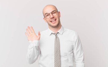 Kel iş adamı mutlu ve neşeli bir şekilde gülümsüyor, el sallıyor, sizi selamlıyor ve selamlıyor, ya da veda ediyor.