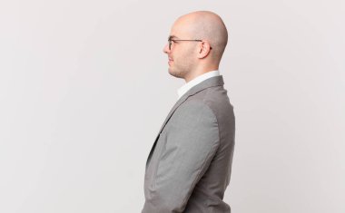 Kel iş adamı profil görünümünde ilerideki boşluğu kopyalamaya çalışıyor, düşünüyor, hayal ediyor ya da hayal kuruyor