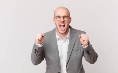 Kel iş adamı öfkeli bir ifadeyle ya da yumruklarıyla başarıyı kutlarken agresif bir şekilde bağırıyor.