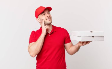 Pizza dağıtan adam mutlu bir şekilde gülümsüyor ve hayal kuruyor ya da şüphe ediyor.