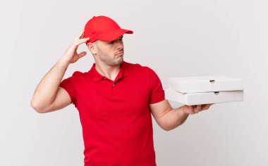 Pizza dağıtan adam şaşkın ve kafası karışmış hissediyor, kafasını kaşıyor ve yan tarafa bakıyor.