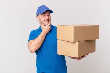Paket teslim adam mutlu, kendinden emin bir ifade ile gülümseyerek çene üzerinde eller, merak ve yan bakıyor