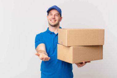 Paket teslimatçısı mutlu bir şekilde güler yüzle, kendinden emin, olumlu bakışla, bir nesne ya da konsept sunarak ve göstererek