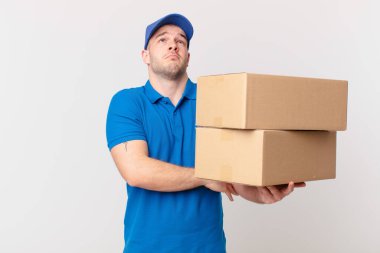 Paket teslimatçısı omuz silkiyor, kafası karışık ve emin değil, kolları bağlı ve şaşkın görünüyor.