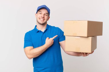 Paket teslim adam neşeli bir şekilde gülümseyerek, mutlu hissediyor ve yan ve yukarı gösteren, kopya uzay nesne gösteren