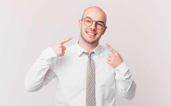лысый бизнесмен уверенно улыбаясь, указывая на свою широкую улыбку, позитивное, расслабленное, удовлетворенное отношение