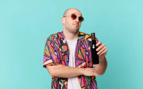 tourist with beer tourist man shrugging, feeling confused and uncertain, doubting with arms crossed and puzzled look