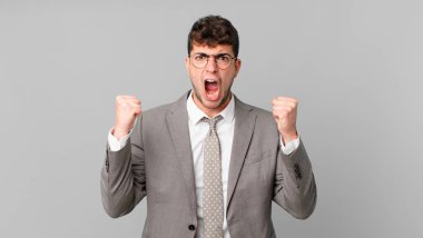 İş adamı kızgın bir ifadeyle ya da yumruklarıyla başarıyı kutlarken agresif bir şekilde bağırıyor.