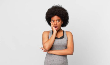 Siyah afro kadın şok ve inançsızlık içinde, elleri yanak ve kolları çapraz, sersemlemiş ve şaşkın hissediyor