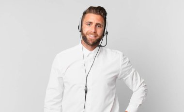 Genç yakışıklı adam mutlu bir şekilde gülümsüyor, eli kalçasında ve kendinden emin. tele pazarlama kavramı