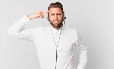 Genç yakışıklı adam kafası karışık ve şaşkın hissediyor, deli olduğunu gösteriyor. tele pazarlama kavramı