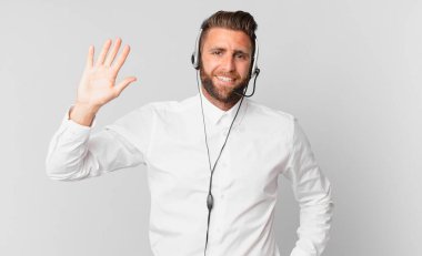 Genç yakışıklı adam mutlu bir şekilde gülümsüyor, el sallıyor, sizi selamlıyor ve selamlıyor. tele pazarlama kavramı