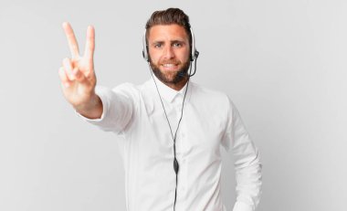 Genç yakışıklı adam gülümsüyor ve arkadaş canlısı görünüyor, iki numarayı gösteriyor. tele pazarlama kavramı