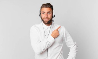 Genç yakışıklı adam neşeyle gülümsüyor, mutlu hissediyor ve bir tarafı işaret ediyor. tele pazarlama kavramı