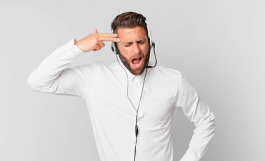 Genç yakışıklı adam mutsuz ve stresli görünüyor, intihar jesti silah işareti yapıyor. tele pazarlama kavramı