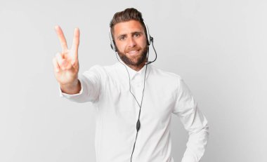 Genç yakışıklı adam gülümsüyor ve mutlu görünüyor, zafer ya da barış işareti yapıyor. tele pazarlama kavramı