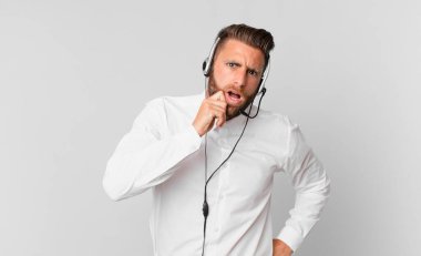 Ağzı ve gözleri açık ve eli çenesinde genç yakışıklı bir adam. tele pazarlama kavramı