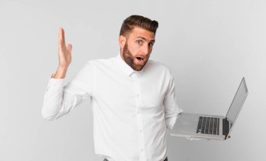 Genç yakışıklı adam kendini mutlu hissediyor ve inanılmaz bir şey karşısında hayrete düşüyor ve elinde bir dizüstü bilgisayar tutuyor.