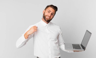 Genç yakışıklı adam kibirli, başarılı, pozitif ve gururlu görünüyor ve elinde bir dizüstü bilgisayar var.