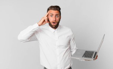 Genç yakışıklı adam şaşırmış görünüyor, yeni bir düşünce, fikir ya da konsept buluyor ve elinde bir dizüstü bilgisayar tutuyor.