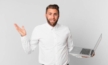 Genç yakışıklı adam mutlu, şaşırmış bir şekilde bir çözüm ya da fikir buluyor ve elinde dizüstü bilgisayar tutuyor.