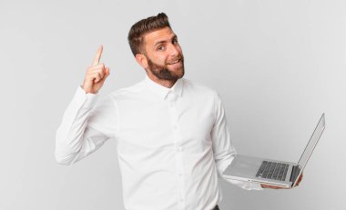 Genç yakışıklı bir adam bir fikri fark ettikten ve dizüstü bilgisayarını tutduktan sonra mutlu ve heyecanlı bir dahi gibi hissediyor.