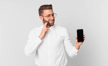 Genç yakışıklı adam mutlu bir şekilde gülümsüyor ve hayal kuruyor ya da şüphe ediyor ve bir hücreyi tutuyor