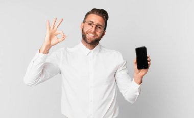 Genç yakışıklı adam kendini mutlu hissediyor. Onaylıyor. İyi bir jest yapıyor ve hücresini tutuyor.