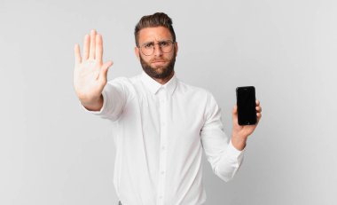 Genç ve yakışıklı adam ciddi görünüyor. Avuç içi gösteriyor. Jesti durduruyor ve elinde bir hücre tutuyor.