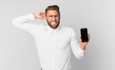 Genç, yakışıklı bir adam kendini stresli, endişeli ya da korkmuş hissediyor. Elleri başının üstünde ve elinde bir hücre tutuyor.