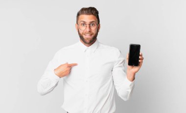 Genç ve yakışıklı bir adam mutlu hissediyor ve heyecanlı bir hücreyle kendini işaret ediyor.