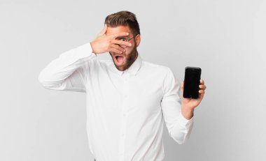 Genç, yakışıklı adam şok olmuş, korkmuş ya da korkmuş görünüyor, yüzünü eliyle kapatıyor ve hücresini tutuyor.