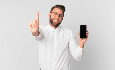 Genç yakışıklı adam gururla gülümsüyor ve kendine güvenerek bir numara oluyor ve elinde bir hücre tutuyor.