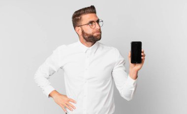 Genç yakışıklı adam omuz silkiyor, kafası karışık ve kararsız ve hücresini tutuyor.