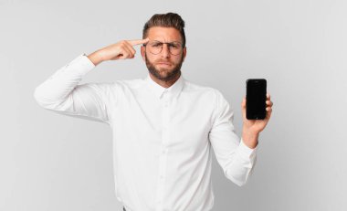 Genç yakışıklı adam şaşkın ve şaşkın hissediyor, deli olduğunu gösteriyor ve elinde bir hücre tutuyor.