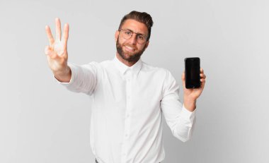 Genç yakışıklı adam gülümsüyor ve arkadaş canlısı görünüyor, üç numarayı gösteriyor ve elinde bir hücre tutuyor.