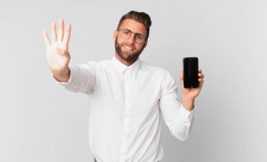 Genç yakışıklı adam gülümsüyor ve arkadaş canlısı görünüyor, dört numarayı gösteriyor ve elinde bir hücre tutuyor.