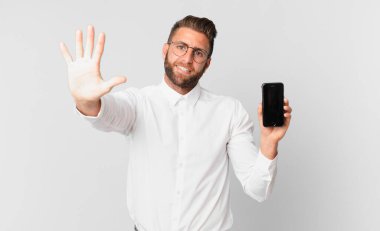 Genç yakışıklı adam gülümsüyor ve arkadaş canlısı görünüyor, beş numarayı gösteriyor ve elinde bir hücre tutuyor.