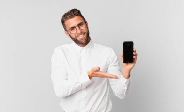 Genç yakışıklı adam neşeyle gülümsüyor, mutlu hissediyor ve bir konsept gösteriyor ve bir hücre tutuyor.