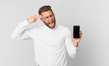 Genç yakışıklı adam mutsuz ve stresli görünüyor, intihar jesti silah işareti yapıyor ve elinde bir hücre tutuyor.