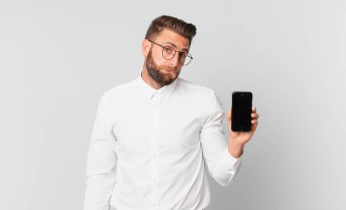 Kafası karışmış, kafası karışmış ve elinde hücresi olan genç yakışıklı bir adam.