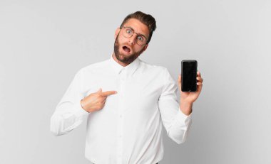 Şok olmuş ve ağzı açık, kendini gösteren ve hücresini tutan genç ve yakışıklı bir adam.