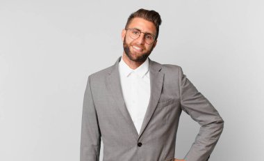 Genç yakışıklı adam mutlu bir şekilde gülümsüyor, eli kalçasında ve kendinden emin. iş kavramı