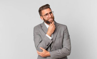 Genç ve yakışıklı bir adam mutlu ve kendinden emin bir ifadeyle gülümsüyor, elleri çenesinde. iş kavramı