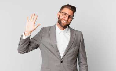 young handsome man smiling happily, waving hand, welcoming and greeting you. business concept