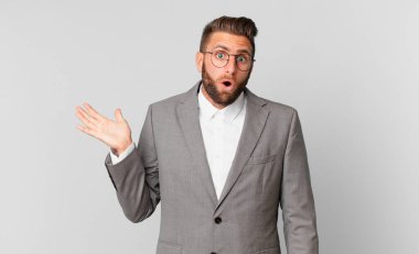 Genç, yakışıklı adam şaşırmış ve şok olmuş görünüyor. Çenesi düşmüş, elinde bir nesne var. iş kavramı