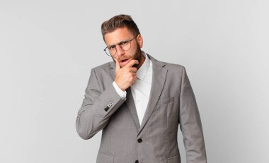 Ağzı ve gözleri açık ve eli çenesinde genç yakışıklı bir adam. iş kavramı