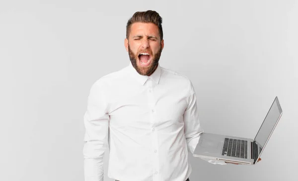 Mladý Pohledný Muž Křičí Agresivně Vypadá Velmi Rozzlobeně Drží Notebook — Stock fotografie