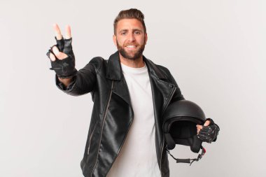 Genç yakışıklı adam gülümsüyor ve mutlu görünüyor, zafer ya da barış işareti yapıyor. Motosiklet kaskı konsepti