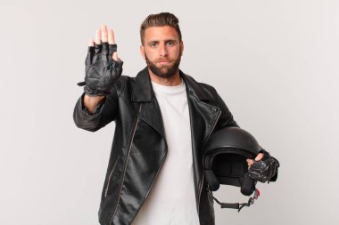 Genç ve yakışıklı adam ciddi görünüyor. Avuç içi gösteriyor. Durdurma hareketi yapıyor. Motosiklet kaskı konsepti